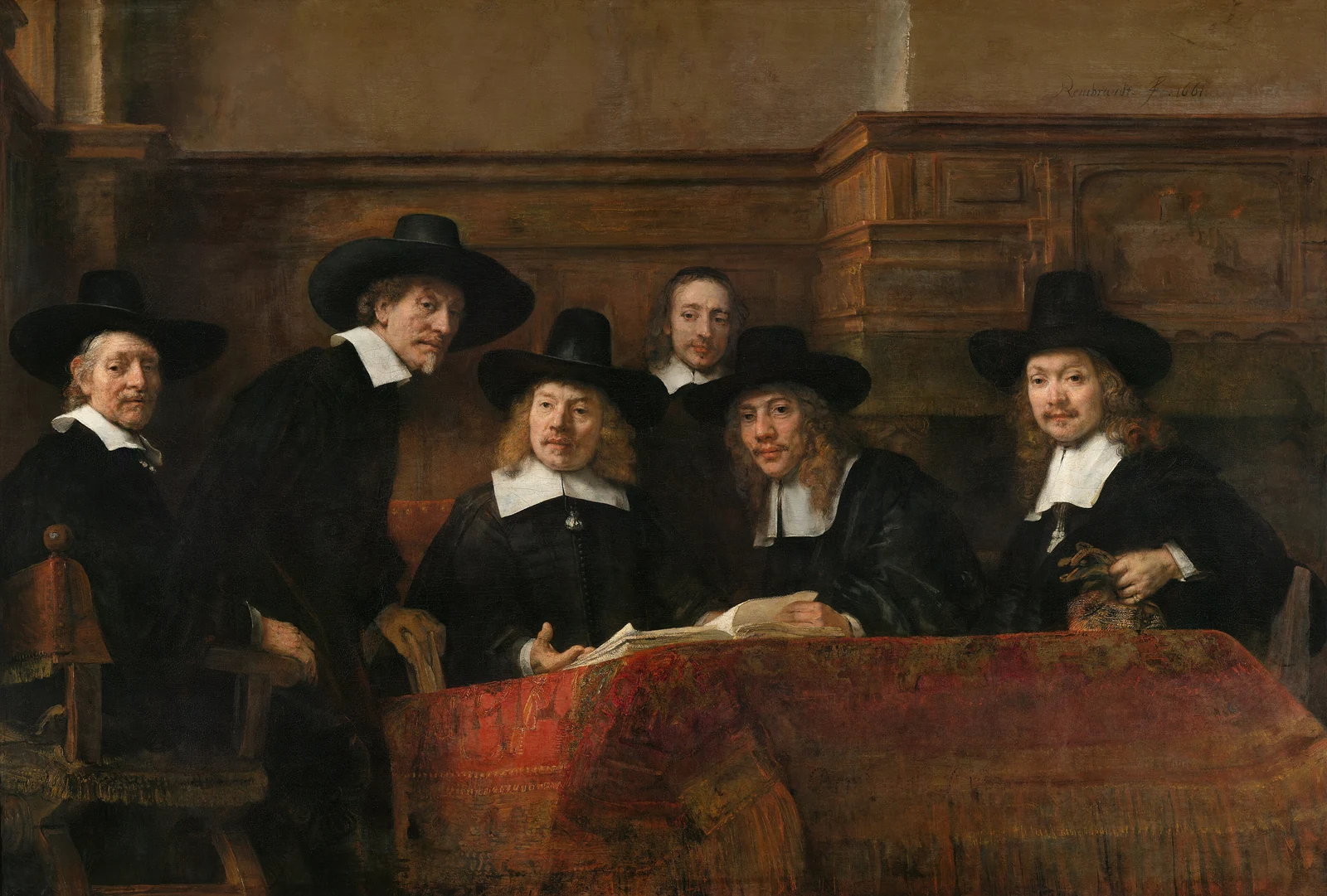 Six men in dark clothing gather around a table covered with a red carpet and an open book.